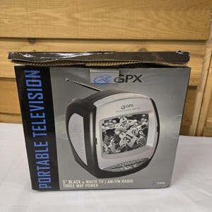 May include: A black and white portable television with a 5-inch screen, AM/FM radio, and three-way power. The TV is in its original box, which has the words "PORTABLE TELEVISION" printed on it. The screen displays a black and white image of a football game.