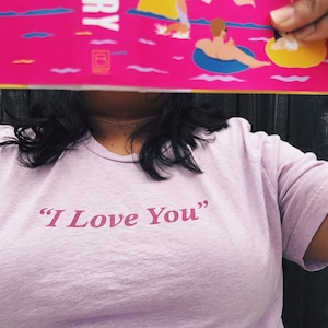 May include: A person wearing a light pink t-shirt with the text "I Love You" printed in pink.