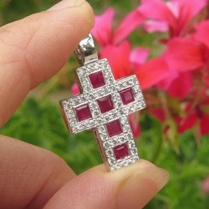 May include: A silver cross pendant with red square gemstones set in a white metal frame.