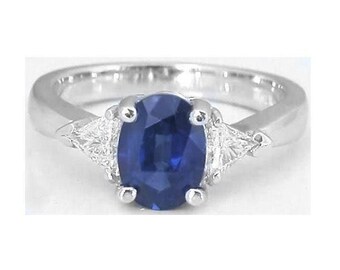 May include: A silver-toned ring featuring a central oval-cut deep blue sapphire gemstone held by four prongs, flanked on each side by a single triangular-cut clear white diamond, all set on a polished metallic band with a smooth, tapered finish.