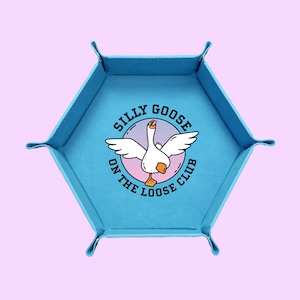 May include: A light blue, hexagonal tray with a raised edge and corner tabs. The center features a cartoon goose with outstretched wings inside a circle, with the text "SILLY GOOSE ON THE LOOSE CLUB" around it.