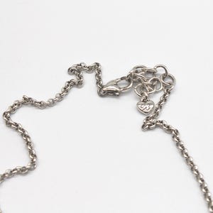 Puede incluir: Primer plano de un collar plateado con una cadena delicada. El collar presenta un cierre de mosquet&oacute;n y un peque&ntilde;o dije en forma de coraz&oacute;n con las iniciales "B3". La cadena es visible sobre un fondo blanco.