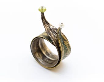 May include: A silver ring with a twisted design resembling leaves, accented with a green and a white gemstone.