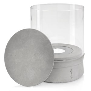 May include: A gray concrete candle lantern with a clear glass cylinder and a removable lid. The lantern has the word "obest&eacute;" printed on the side.