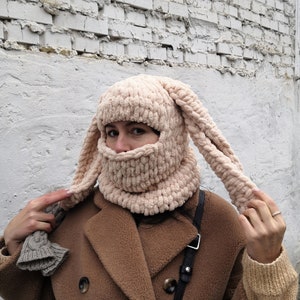 Puede incluir: Un pasamonta&ntilde;as beige tejido con largas orejas de conejo flexibles. La cobertura facial tiene una textura acanalada y se usa con un abrigo marr&oacute;n. El sombrero es un accesorio &uacute;nico hecho a mano.