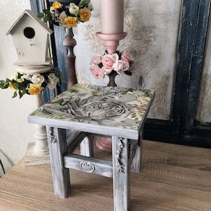 May include: A small white wooden stool with a gray wash finish and a decorative tiger print top. The stool has a distressed look and is perfect for adding a touch of rustic charm to any room.
