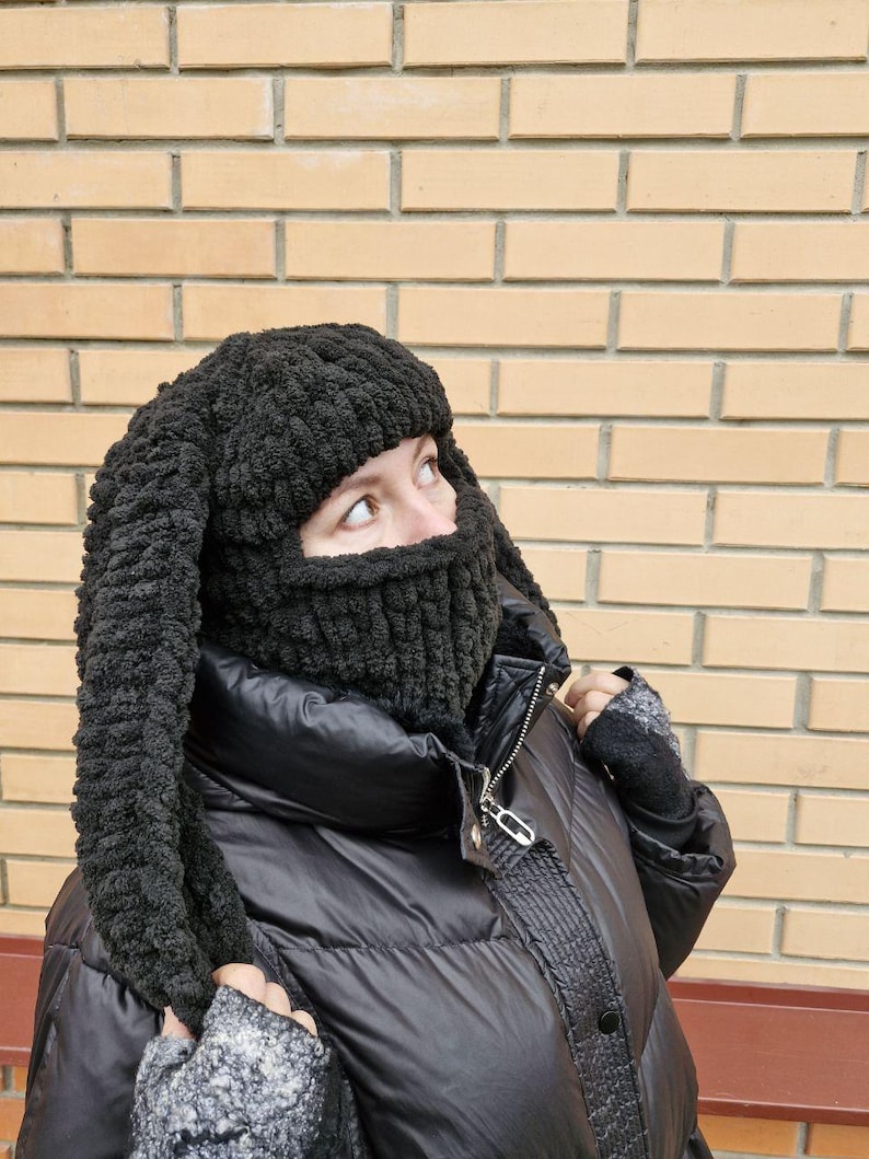 Puede incluir: Un pasamonta&ntilde;as negro tejido con largas orejas de conejo flexibles. La cobertura facial tiene una textura acanalada, y las orejas est&aacute;n hechas de un hilo suave y texturizado. El pasamonta&ntilde;as se usa con una chaqueta acolchada negra.