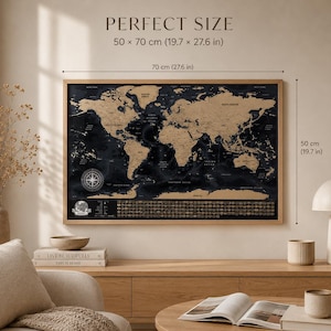 May include: A rectangular scratch-off world map in a light wood frame with black oceans and gold continents. The map features a compass rose and icons at the bottom. Text reads PERFECT SIZE 50 x 70 cm (19.7 x 27.6 in) with dimension lines.