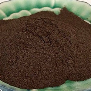 Puede incluir: Primer plano de un pequeño plato de cerámica verde lleno de una gran cantidad de polvo marrón oscuro.