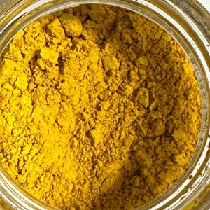 May include: Close-up of a clear glass jar filled with a vibrant yellow powder. The powder has a fine, granular texture and appears to be a spice or pigment. The jar's rim is visible, showing a metallic, aged finish. The overall image suggests a culinary or artistic product.
