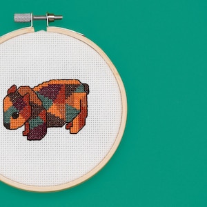 Könnte beinhalten: Ein Kreuzstich-Stickrahmen mit einem farbenfrohen geometrischen Design eines Wombats. Der Wombat ist braun, orange, grün und lila.