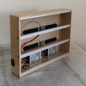 以下が含まれることがあります： 3つの棚がある木製の電子機器エンクロージャ。各棚には黒いコンポーネント、配線、銀色のレールが含まれています。下部には2つのファンが見えます。電源スイッチは側面にあります。