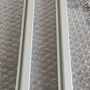 May include: Two long, white metal tracks with a groove running down the center. The tracks are parallel to each other, resting on a bubble wrap surface. The tracks are likely for a sliding door or window.