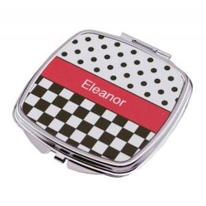 May include: A silver compact mirror with a checkered and polka dot design. The mirror has a red band with the name "Eleanor" printed on it.