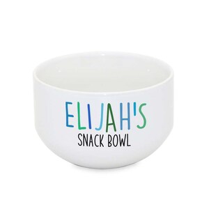 Puede incluir: Taz&oacute;n de cer&aacute;mica blanco con el texto "ELIJAH'S SNACK BOWL" en letras de colores.