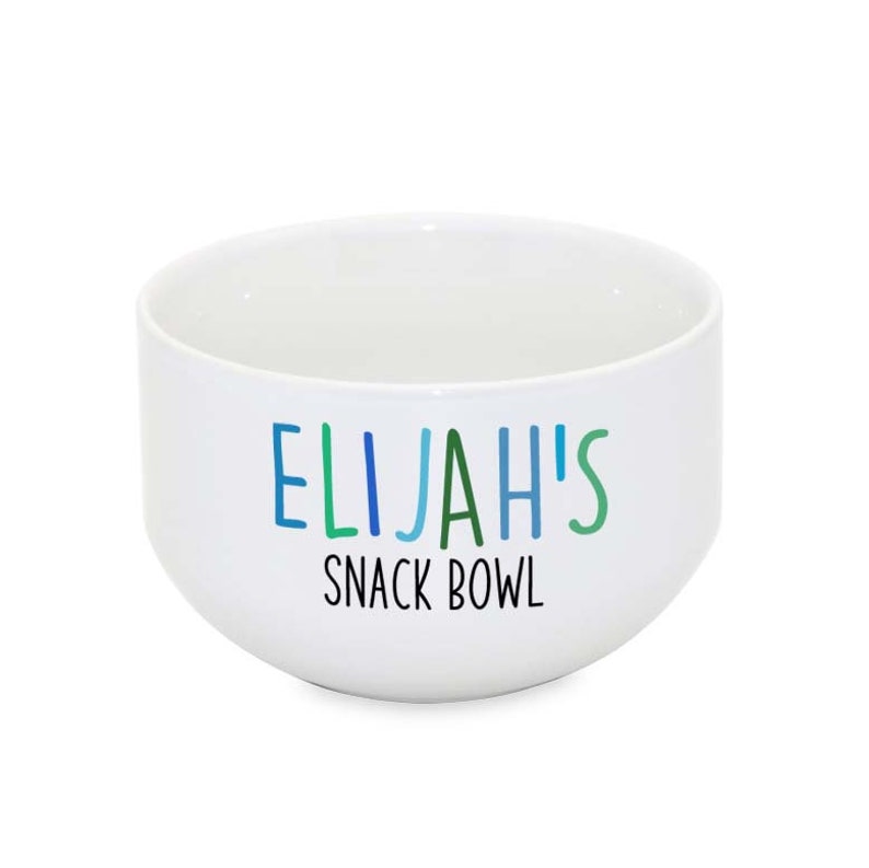 Puede incluir: Taz&oacute;n de cer&aacute;mica blanco con el texto "ELIJAH'S SNACK BOWL" en letras de colores.