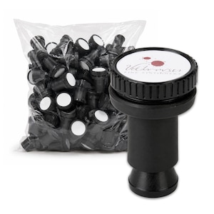 May include: A black plastic bottle stopper with a circular top featuring a white label with red ink splatters and the text Vildmser Fine Stationery. A clear plastic bag filled with multiple identical black bottle stoppers is positioned behind it.