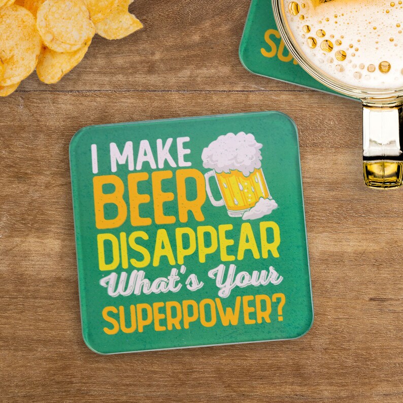 May include: Green square coaster with a yellow and white beer mug graphic and the text "I make beer disappear. What's your superpower?"