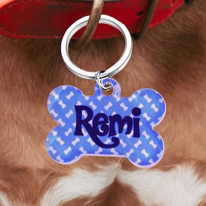 May include: Blue bone-shaped dog tag with white bone pattern and the name "Remi" in dark blue lettering.