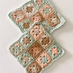 Könnte beinhalten: Zwei gehäkelte Quadrate in Granny-Square-Muster. Die Quadrate sind aus beige, hellgrünem und rosafarbenem Garn gefertigt.
