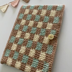 Könnte beinhalten: Eine gehäkelte Tasche in beige, creme und grün mit Karomuster und einem Knopfverschluss.