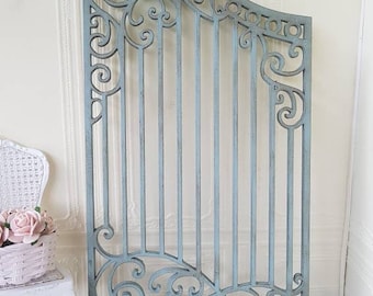 May include: A decorative metal gate with a blue-grey finish and intricate scrollwork. The gate is made of thin metal bars and has a curved top.