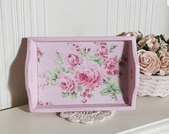 May include: A pink wooden tray with a floral design featuring pink roses and green leaves. The tray has a white crocheted doily underneath it.