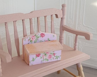 May include: A small wooden box with a floral design on the front and sides. The box is sitting on a pink wooden bench.