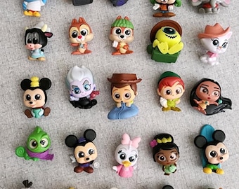 Puede incluir: Una colección de pequeñas figuras de personajes coloridos, incluyendo Mickey Mouse, Stitch y otros personajes animados populares. Las figuras están dispuestas sobre una superficie gris claro, mostrando una variedad de diseños y poses.