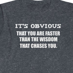 Puede incluir: Camiseta gris oscuro con texto blanco: "IT'S OBVIOUS THAT YOU ARE FASTER THAN THE WISDOM THAT CHASES YOU."