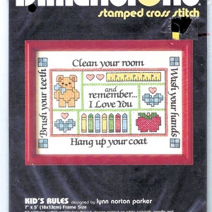 May include: A cross stitch pattern titled "Kid's Rules" with a colorful design featuring a teddy bear, crayons, an apple, and the text "Clean your room", "Wash your hands", "Brush your teeth", "Remember... I love you", and "Hang up your coat".
