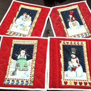 May include: Four red quilted pot holders with white trim, each featuring a different snowman design. The snowmen are depicted in a winter scene with a blue background and white snow.