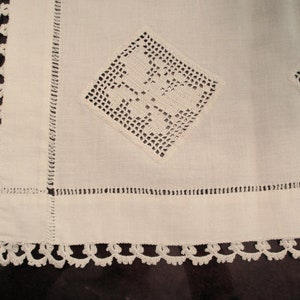 May include: White crocheted table runner with a delicate lace border and two square crocheted designs in the center.