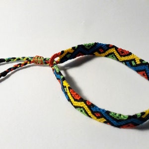 May include: A colorful friendship bracelet with a geometric pattern in shades of red, yellow, green, blue, and black. The bracelet has a simple knot closure.