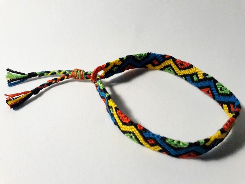 May include: A colorful friendship bracelet with a geometric pattern in shades of red, yellow, green, blue, and black. The bracelet has a simple knot closure.