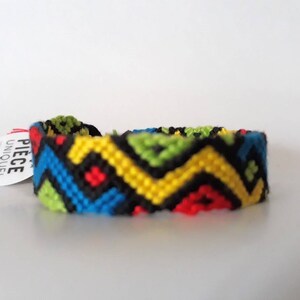 May include: A colorful friendship bracelet with a geometric pattern in black, yellow, blue, green, and red.