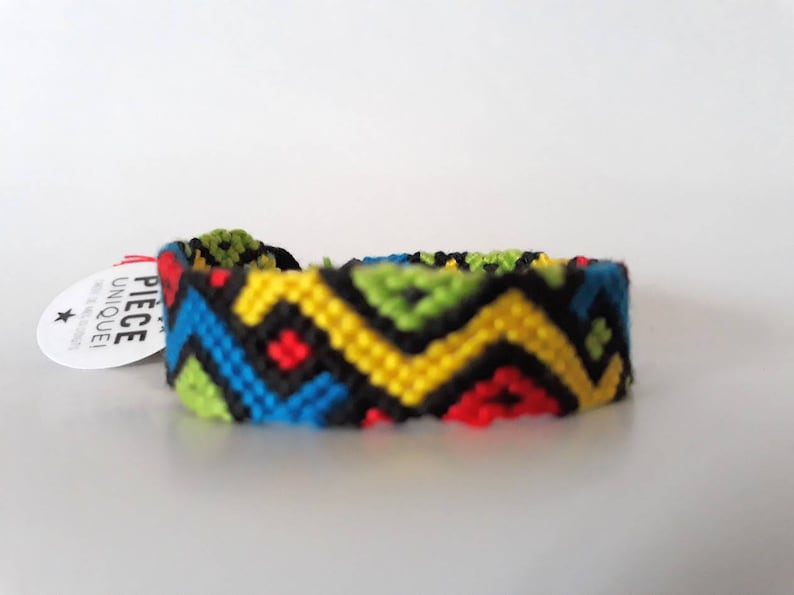 May include: A colorful friendship bracelet with a geometric pattern in black, yellow, blue, green, and red.