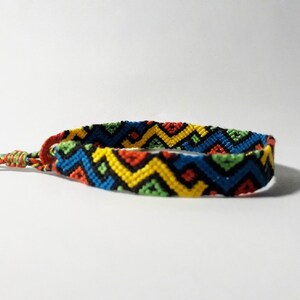 May include: A colorful friendship bracelet with a geometric pattern in shades of red, yellow, blue, green, and black.