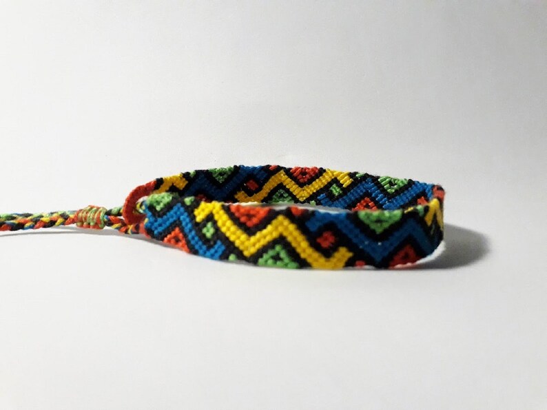 May include: A colorful friendship bracelet with a geometric pattern in shades of red, yellow, blue, green, and black.