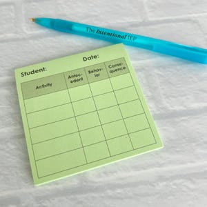 May include: A light green notepad with a grid layout for tracking student behavior, with the text "Student:" and "Activity" at the top. A blue pen with the text "The Intentional IEP" rests on the top.