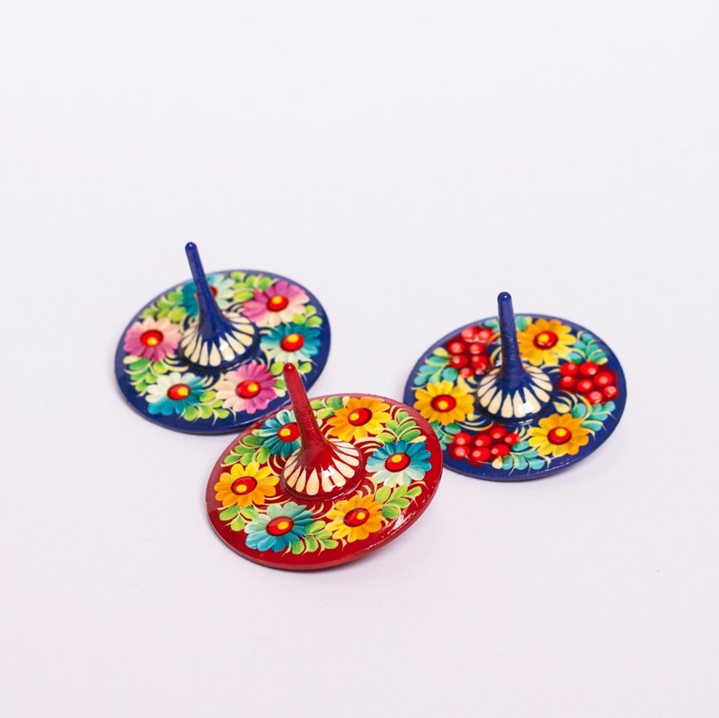 Puede incluir: Tres peonzas de madera con dise&ntilde;os florales coloridos. Las peonzas est&aacute;n pintadas en tonos de azul, rojo y amarillo con intrincados patrones florales.