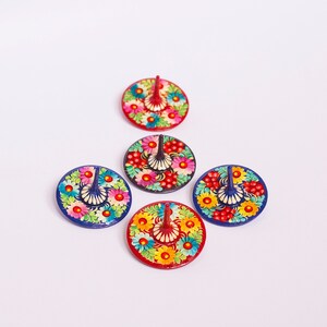 Puede incluir: Cinco peonzas de madera coloridas con dise&ntilde;os florales. Cada peonza tiene una punta puntiaguda y una base circular. Las peonzas est&aacute;n pintadas en tonos de rojo, azul, amarillo, verde y negro.