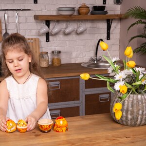 K&ouml;nnte beinhalten: Ein Set aus vier h&ouml;lzernen Matroschka-Puppen mit einem leuchtend gelben und orangen Blumenmuster sowie filigranen roten und wei&szlig;en Details. Die Puppen sind in verschiedenen Stadien des Zusammenbaus zu sehen, die das hohle Innere zeigen.