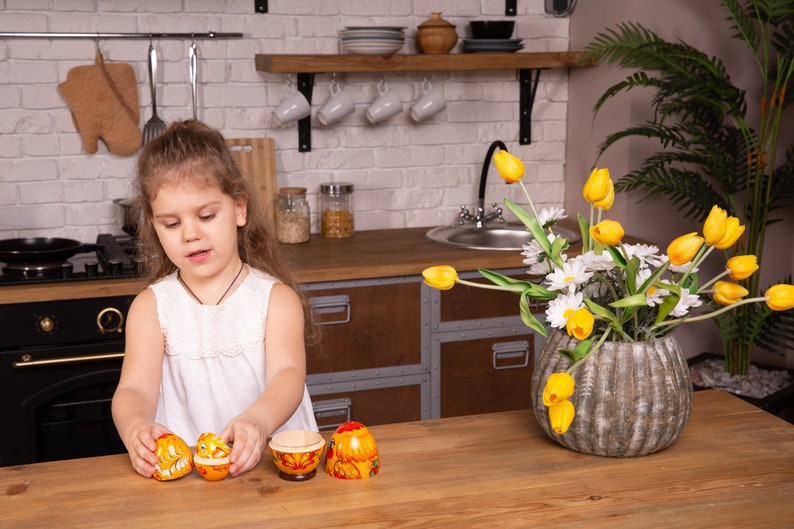K&ouml;nnte beinhalten: Ein Set aus vier h&ouml;lzernen Matroschka-Puppen mit einem leuchtend gelben und orangen Blumenmuster sowie filigranen roten und wei&szlig;en Details. Die Puppen sind in verschiedenen Stadien des Zusammenbaus zu sehen, die das hohle Innere zeigen.