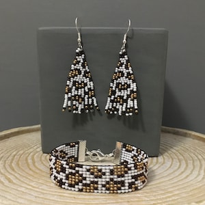 May include: A set of dangle earrings and a bracelet with a geometric pattern of black, white, and gold beads.