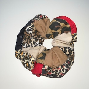 Può includere: Un elastico per capelli patchwork con vari tessuti. Include stampa leopardata, rosso unito, beige e nero. L'elastico è un accessorio per capelli.