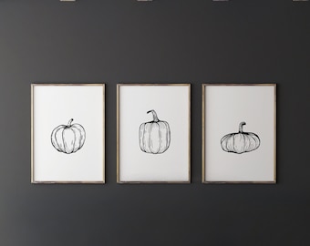 Op de afbeelding: Drie zwart-witte lijntekeningen van pompoenen in eenvoudige frames op een donkergrijze muur.