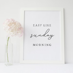 Puede incluir: Impresi&oacute;n enmarcada en blanco con el texto "Easy Like Sunday Morning" en fuente cursiva negra. Una sola hortensia rosa est&aacute; en un jarr&oacute;n de vidrio transparente a la izquierda de la impresi&oacute;n.