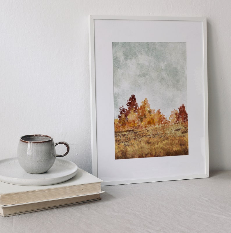 May include: A white framed print of a watercolour painting depicting a field of trees in autumn colours. The trees are mostly yellow and orange with some red and brown hues. The sky is a light blue with some grey clouds.