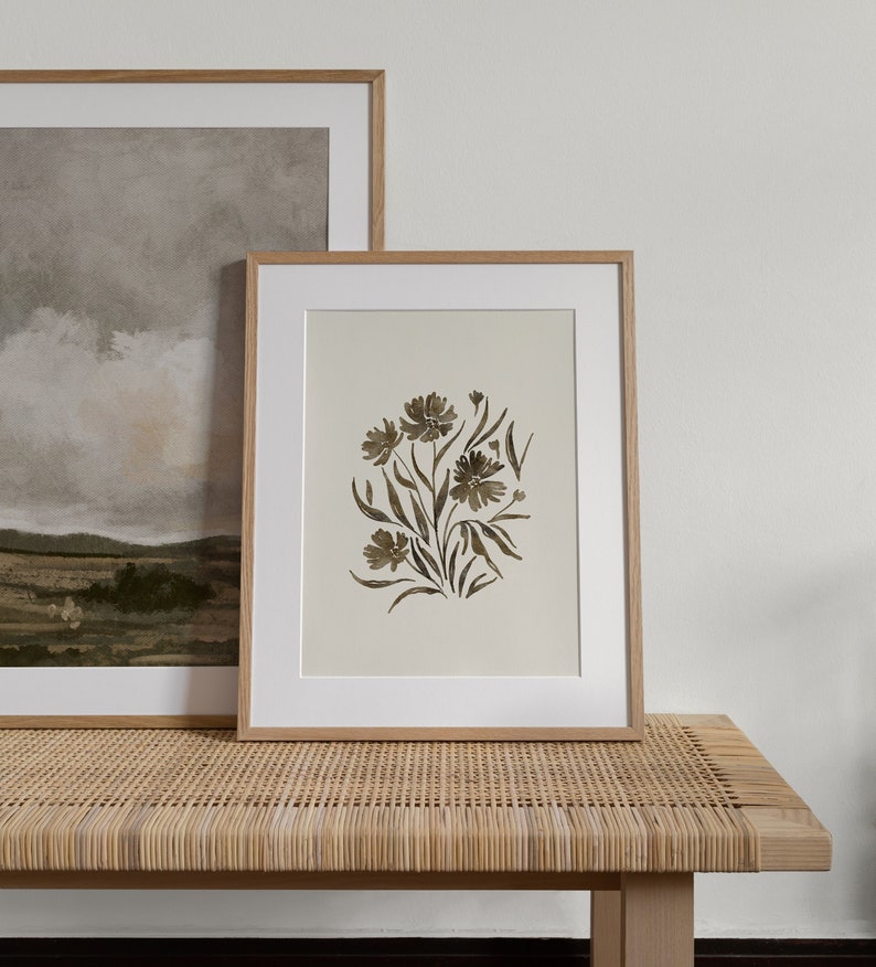 May include: A framed print of a watercolor painting of a bouquet of brown flowers on a white background. The print is in a light wood frame and is sitting on a woven wicker bench.